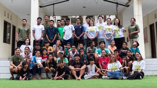 Large group photo of children, Bali Life staff, and the Sunset Eyewear/Tiny Hands Bali team smiling together in the courtyard after the activity